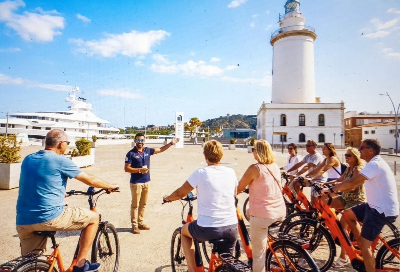 Grupo de personas con bicicletas en un paseo junto a un faro
